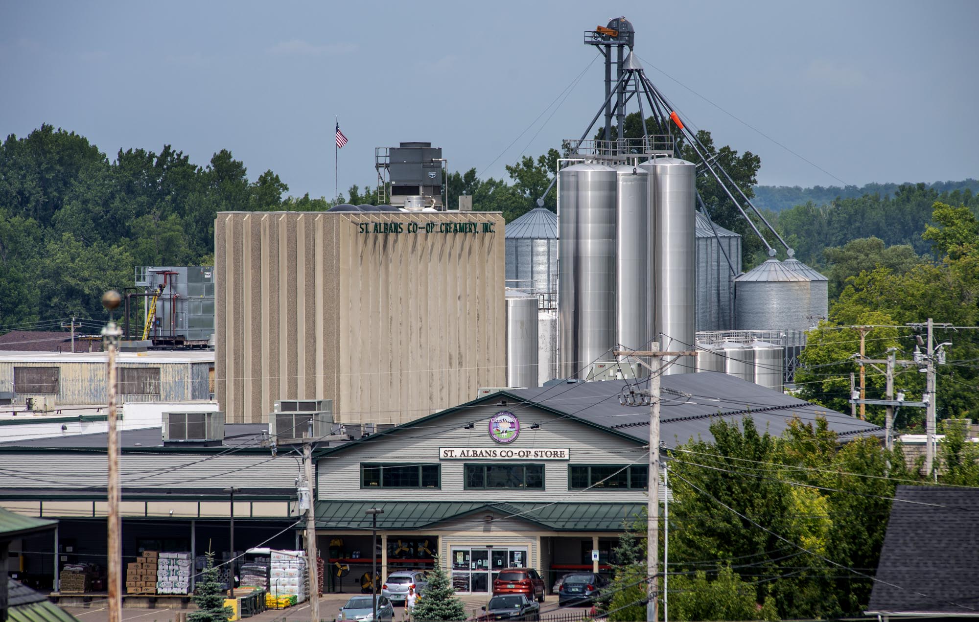 A cooperative store and large grain silos with the sign "St. Albans Co-Op" under a partly cloudy sky, surrounded by trees and power lines.