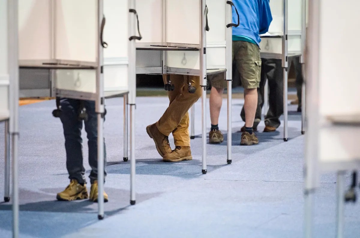 People standing at voting booths, with only their legs visible.