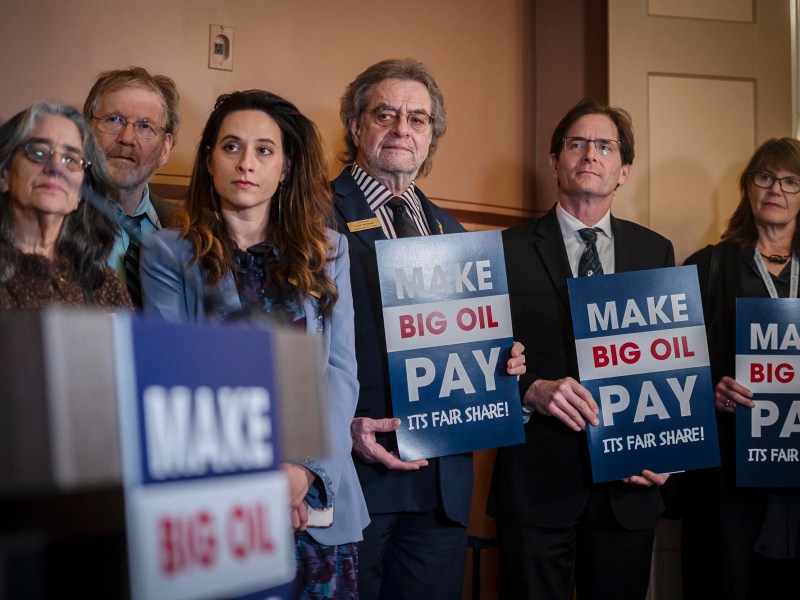 A group of people holding up signs that say make big oil pay.