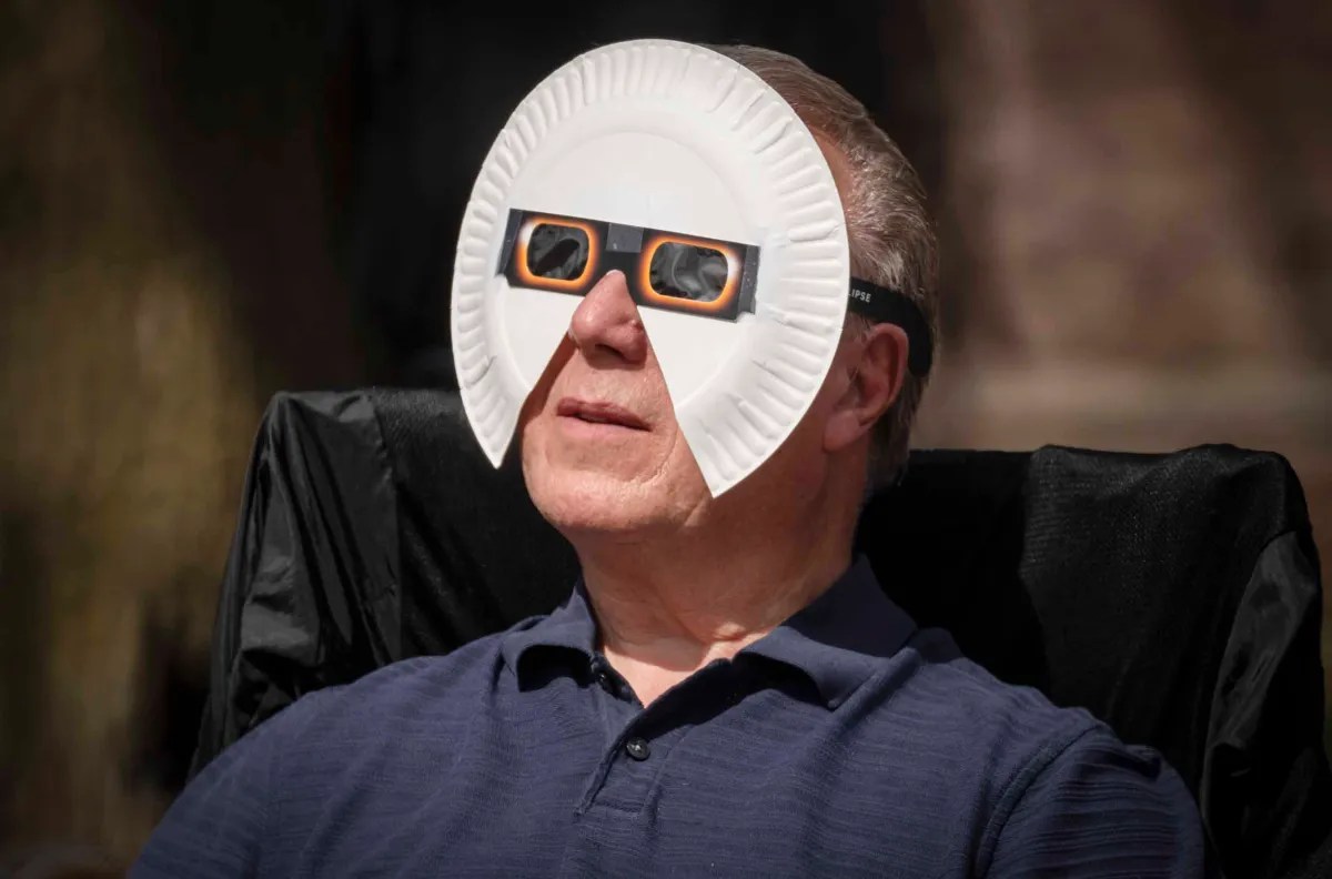A man wearing protective eclipse glasses and sitting comfortably outdoors.