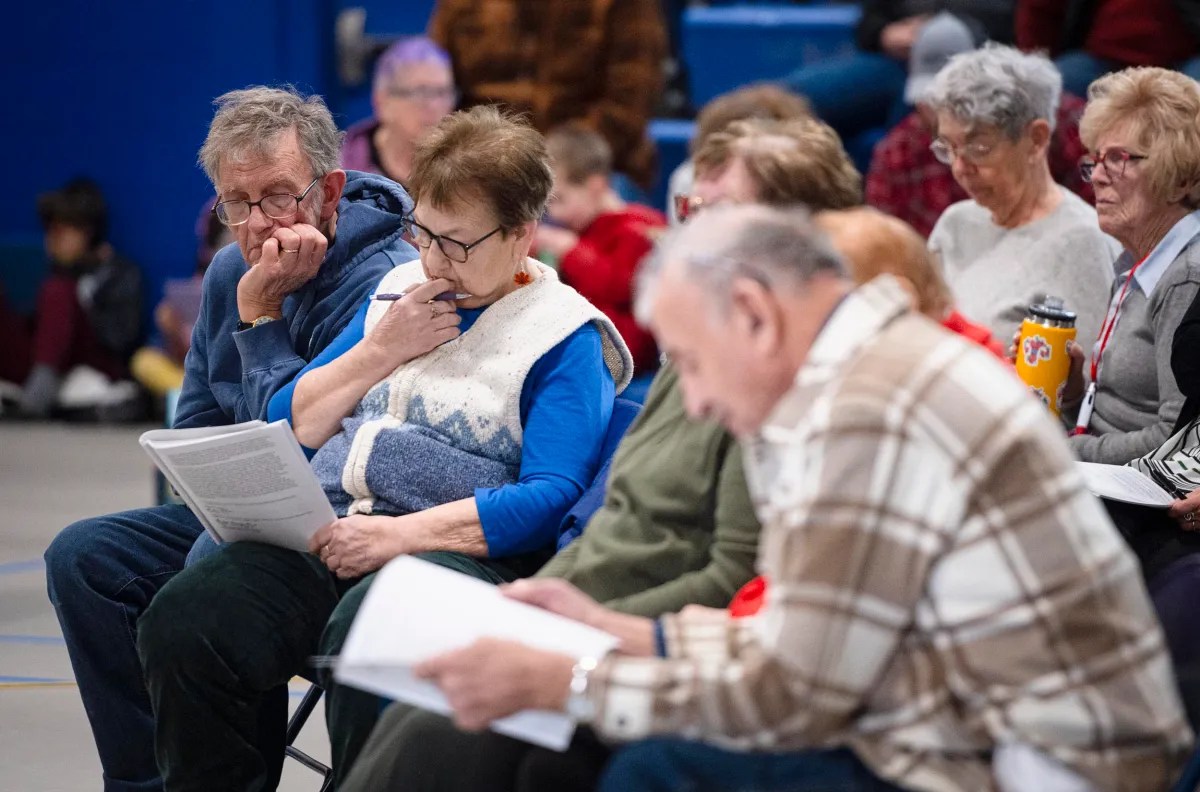 A group of adults seated in chairs, attentively reading and reviewing papers in a community setting.