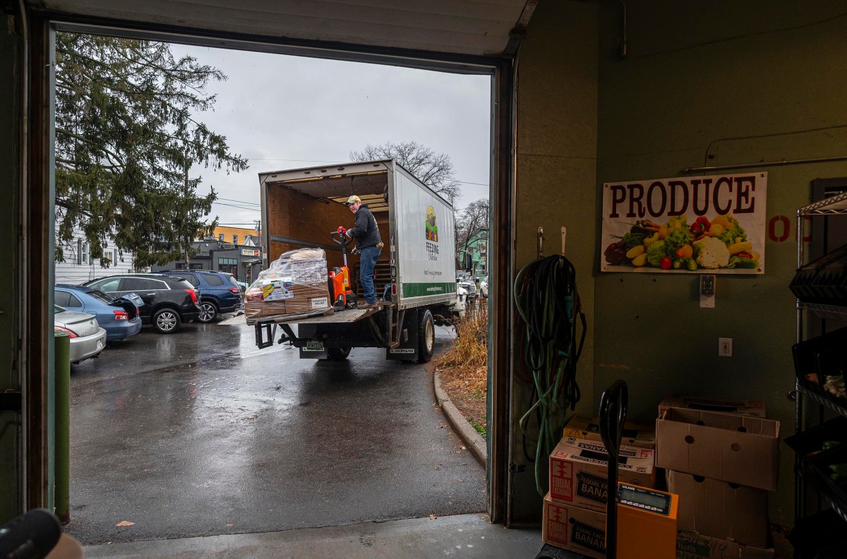 A person unloads pallets from a truck labeled with a produce company logo in a parking lot outside a building on a rainy day.