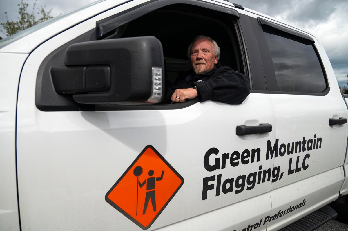 A man sits in the driver's seat of a white Green Mountain Flagging, LLC truck with the company logo visible on the door.