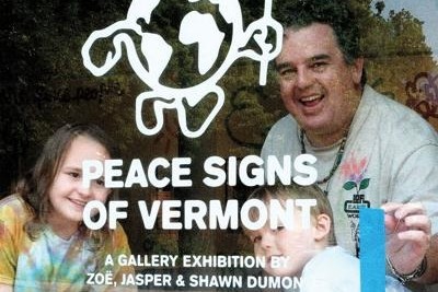 Three people smile behind a window displaying the text "Peace Signs of Vermont: A Gallery Exhibition by Zoë, Jasper & Shawn Dumont" with a peace sign globe graphic.