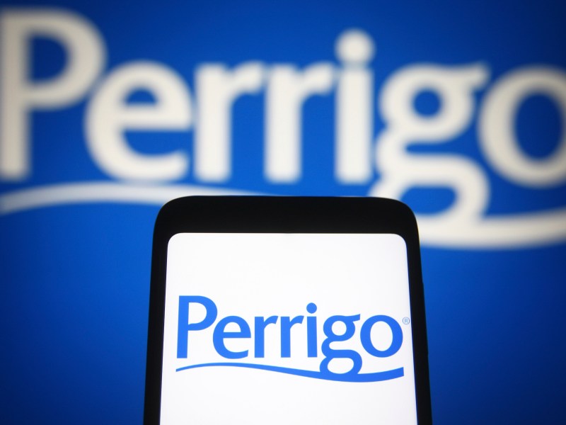 The Perrigo logo displayed on a smartphone screen, with a larger version of the logo blurred in the background.