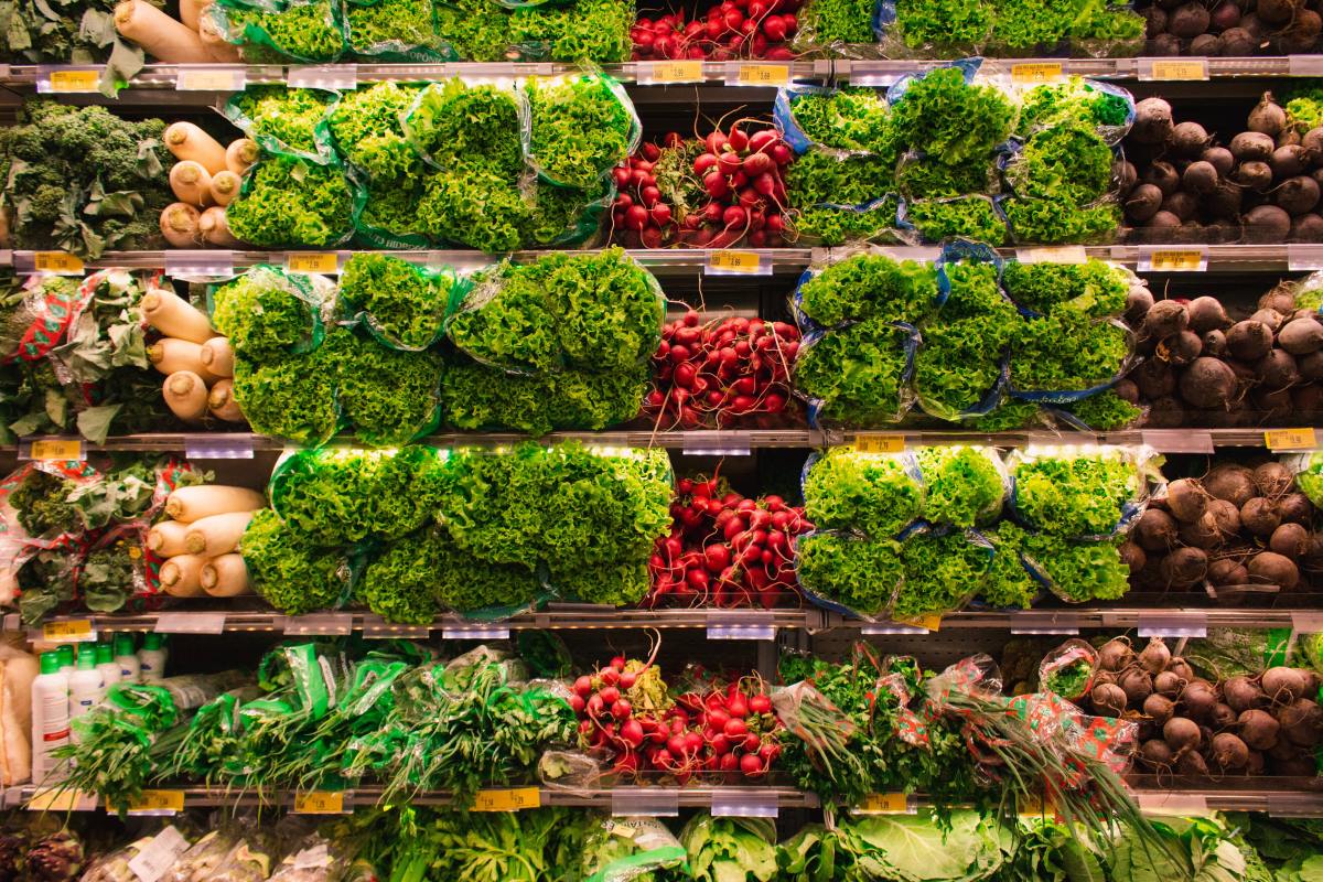 A produce shelf with greens and radishes at a grocery store.