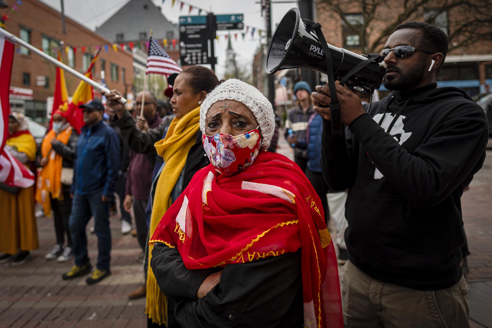 A woman in red clothing and a face covering stands among a protest.