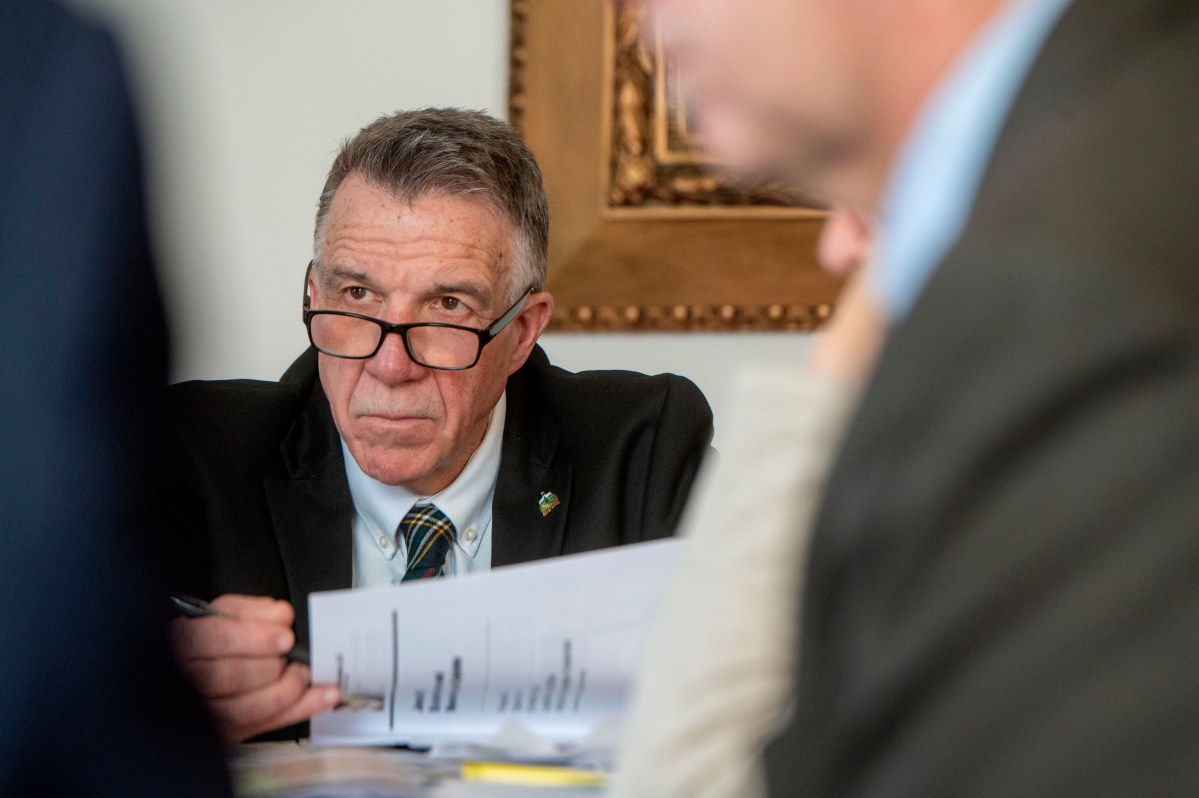 Man with glasses holding papers, appearing focused, in a formal setting.