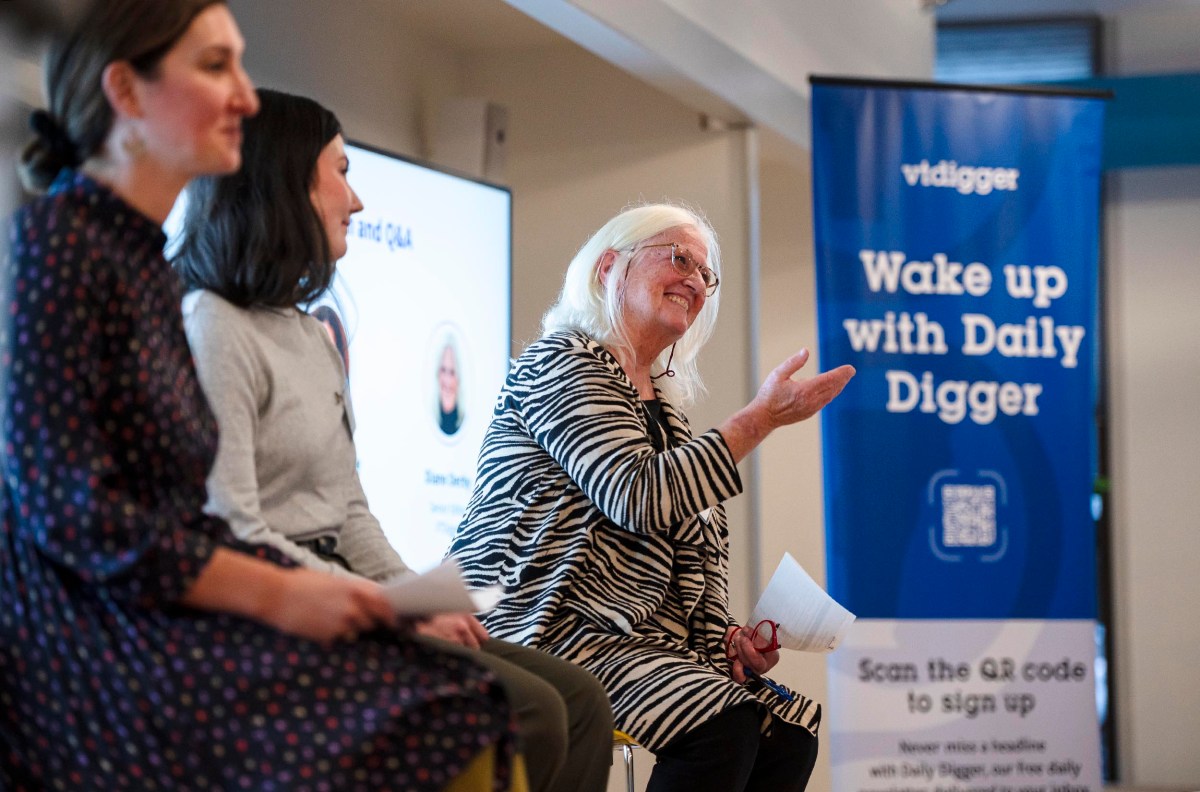 Three women sitting on a panel discussion. One woman gestures with her hand while the others listen. A banner in the background reads "vtdigger - Wake up with Daily Digger.