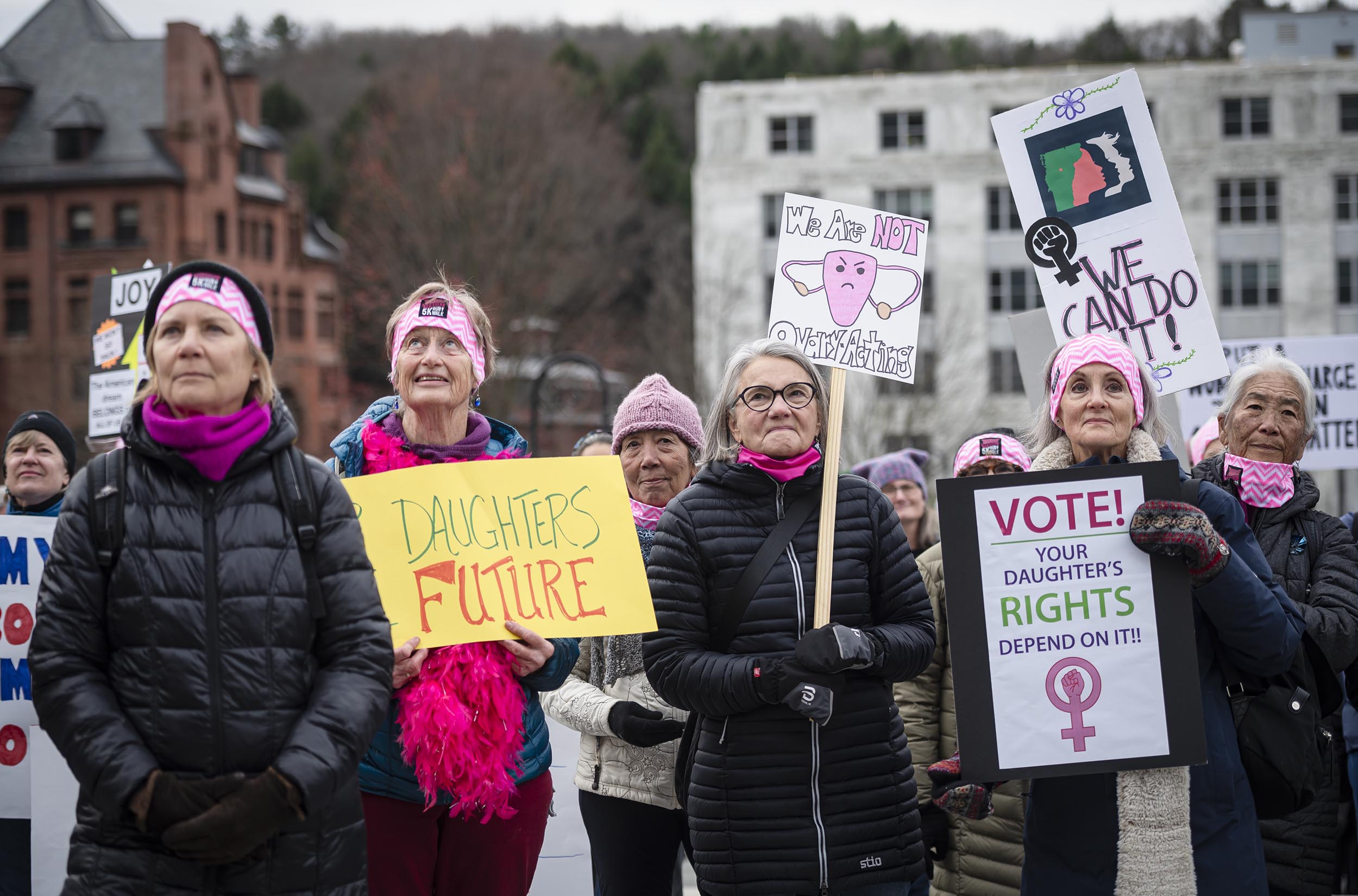 A group of people, mostly women, stand outdoors holding signs advocating for women's and daughters' rights.